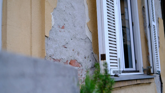 Old building wall with peeling paint and open window shutters.